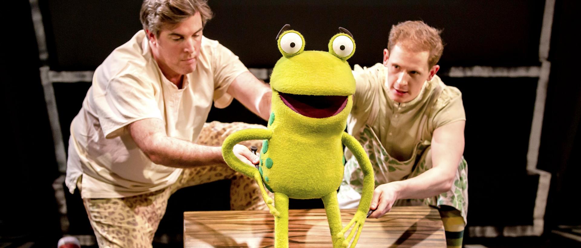 Two puppeteers are operating a green frog puppet.