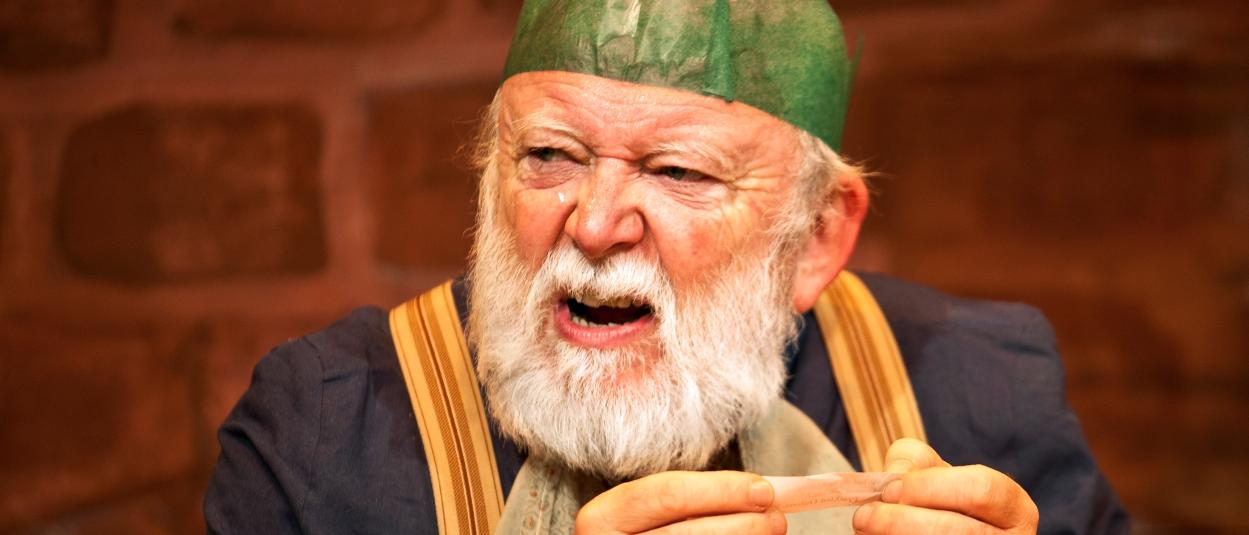 A grumpy Father Christmas reads a joke from a Christmas cracker.