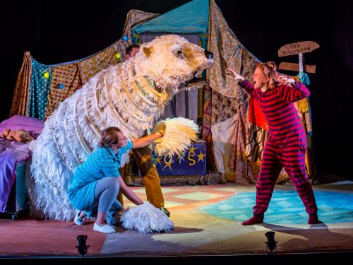 A giant polar bear puppet roars at a young girl. The young girl roars back.