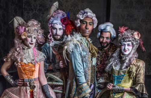 A group of five humans dressed in colourful Georgian wigs and clothes with a modern twist.