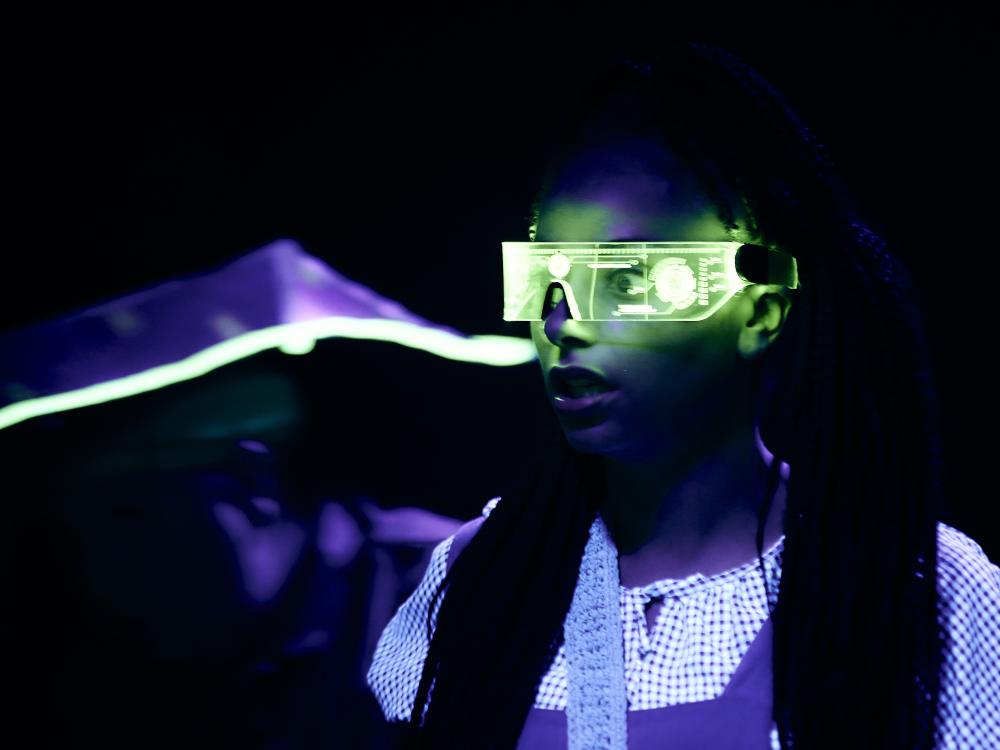 Dorothy is in a dark room, wearing green goggles. Waiting to meet the Wizard of OZ.