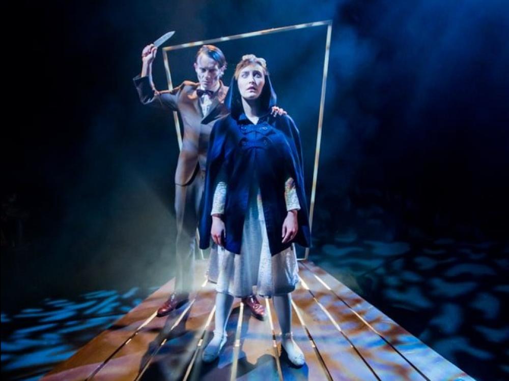 A woman steps through a door in the gloom. A man appears behind her with a knife. He is about to strike.