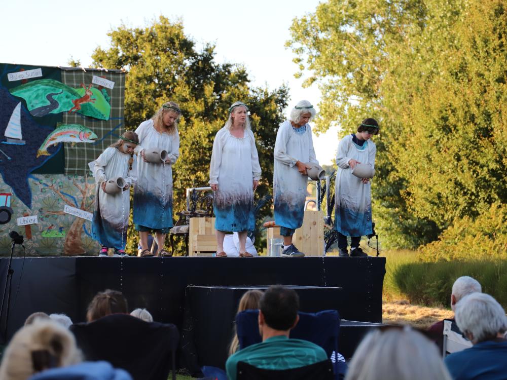 Cast of Rising Waters stand on grass in front of a lake