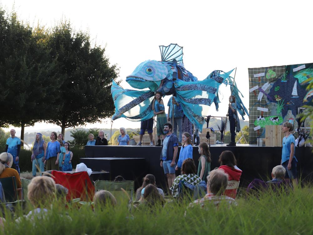 Cast of Rising Waters stand on grass in front of a lake