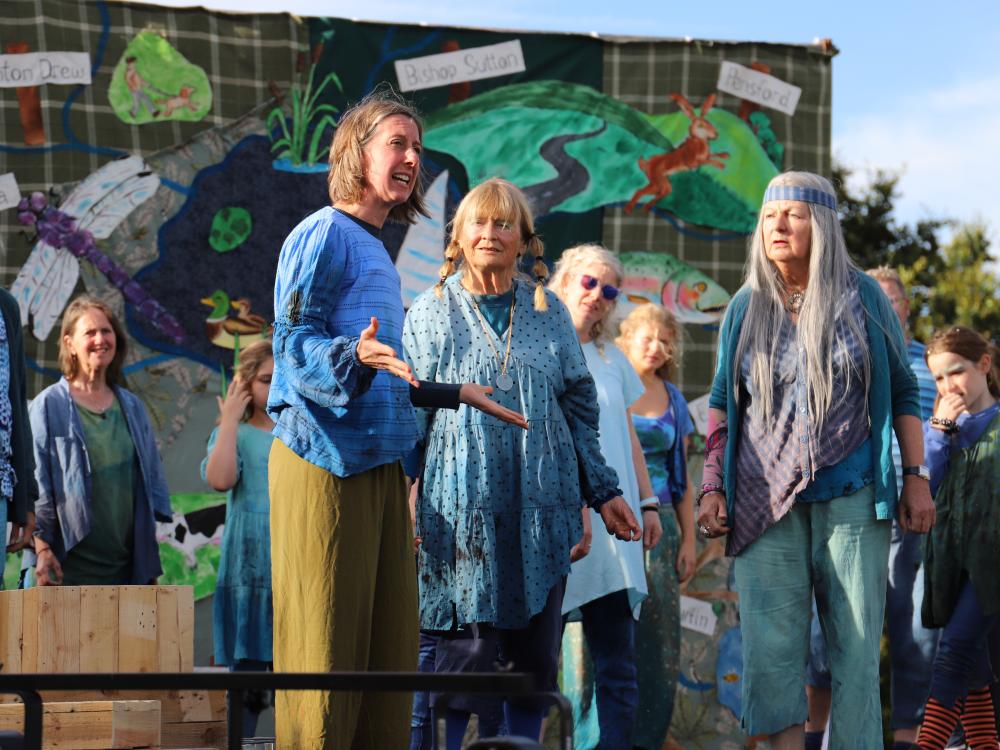 Cast of Rising Waters stand on grass in front of a lake