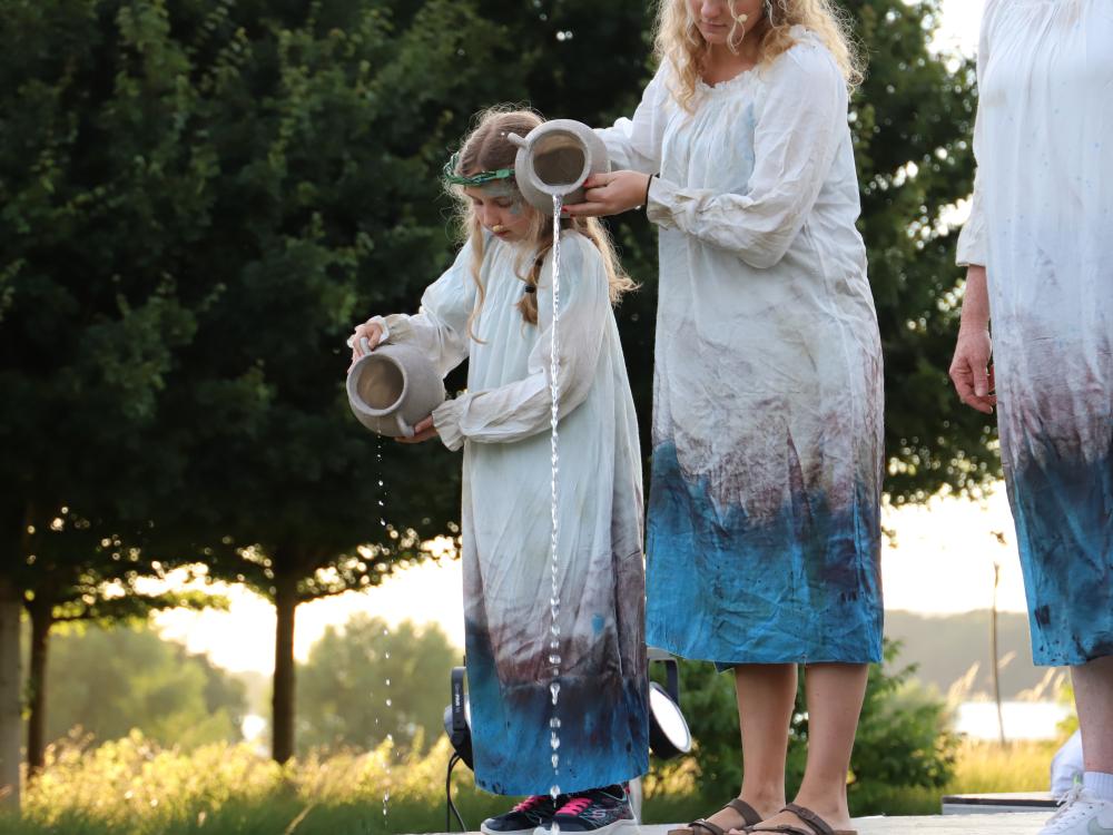 Cast of Rising Waters stand on grass in front of a lake