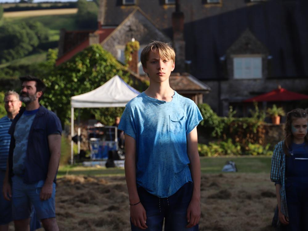 Cast of Rising Waters stand on grass in front of a lake