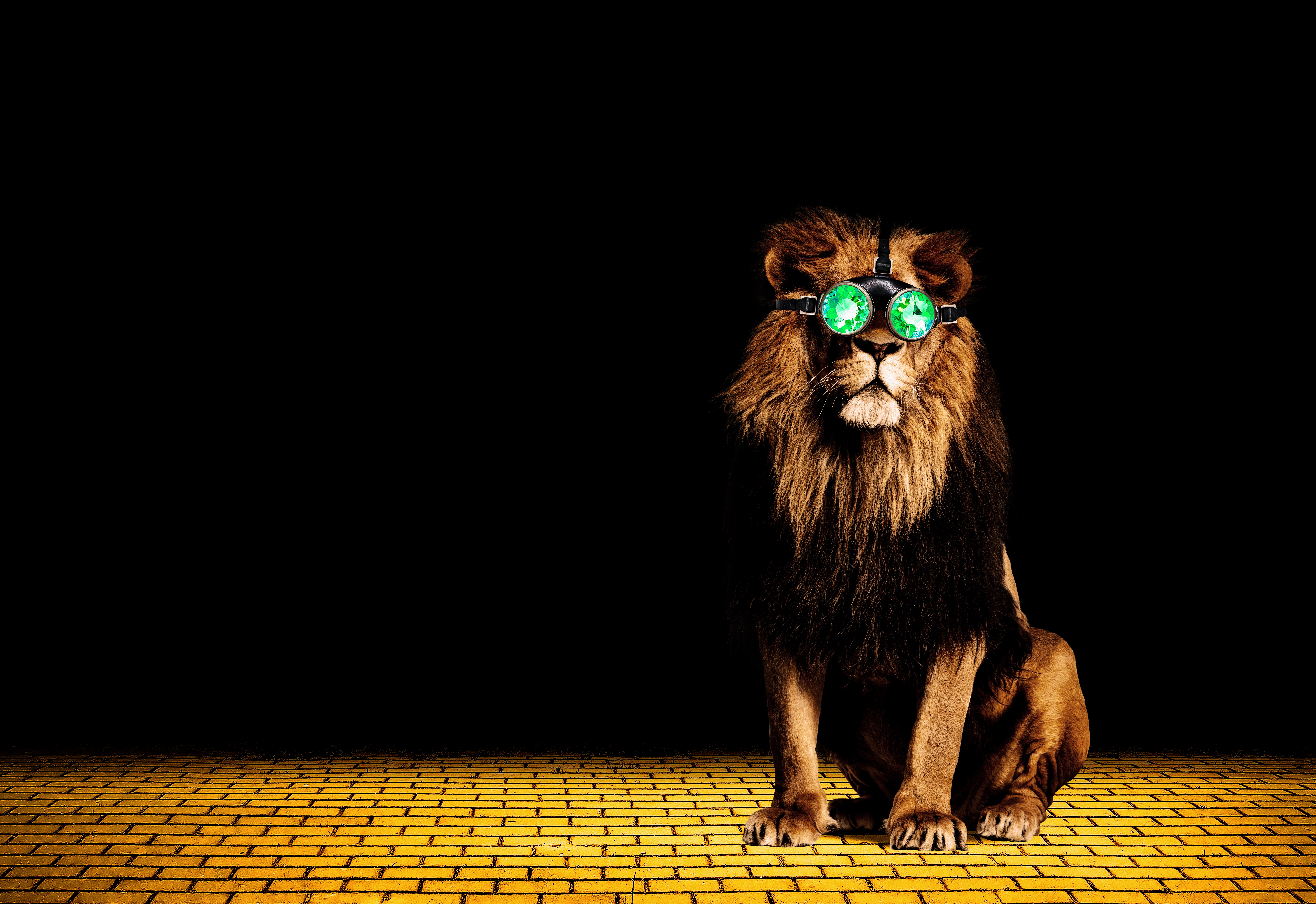 A lion wearing green goggles sits on a yellow brick road.