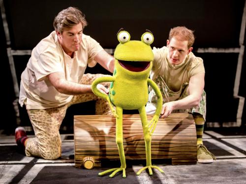 Two puppeteers are operating a green frog puppet.